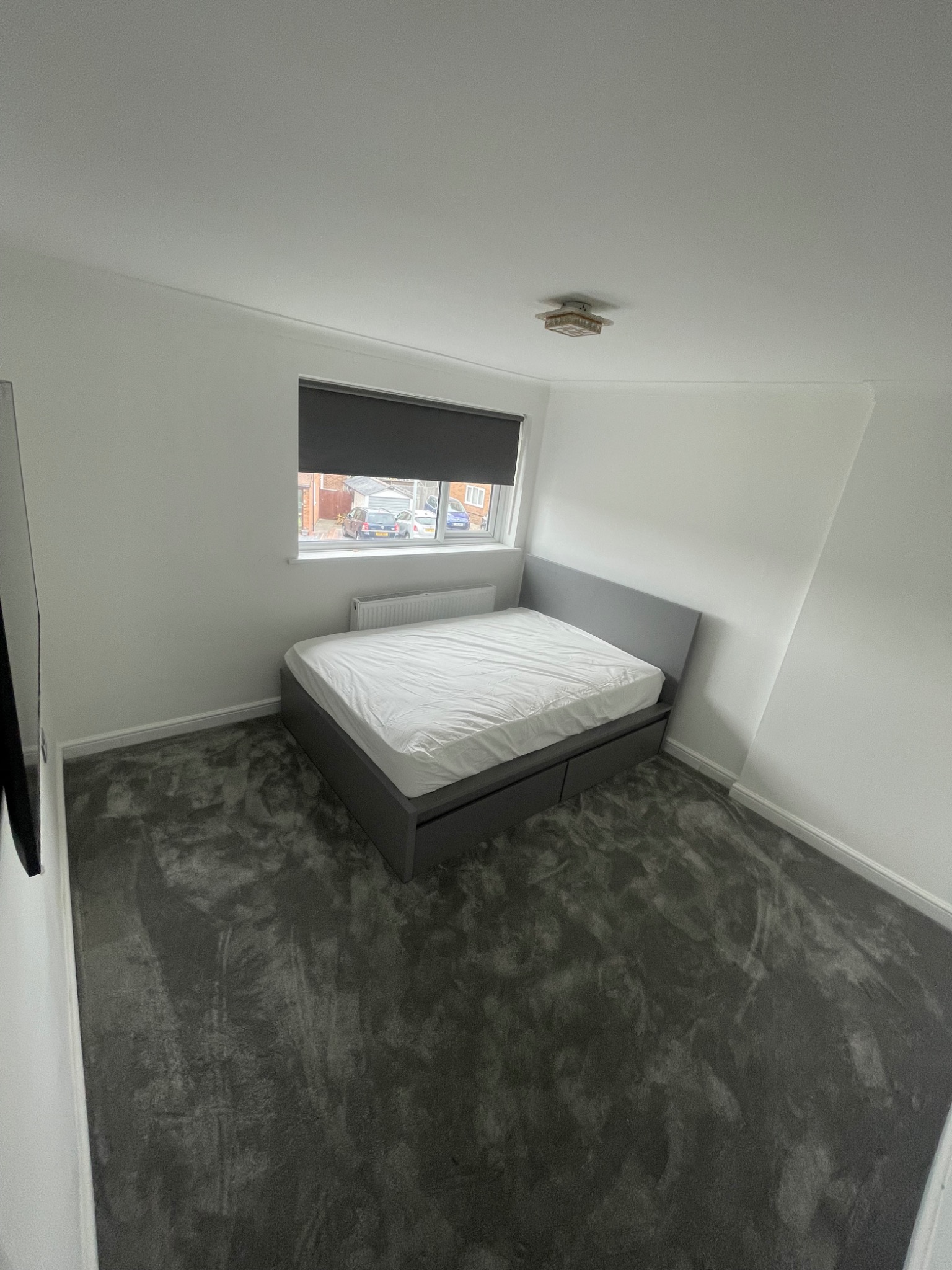 After: a finished bedroom with grey carpet, an assembled bed and a fitted roller blind.